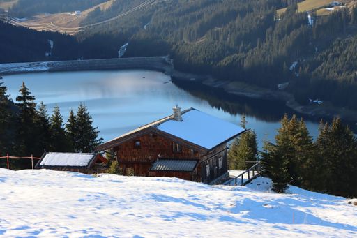 An aerial view of building near lake surrounded by dense trees and snow covered field
