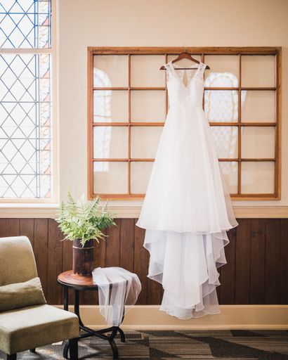 A vertical shot of a white wedding dress hanging on a wall and a veil on a table