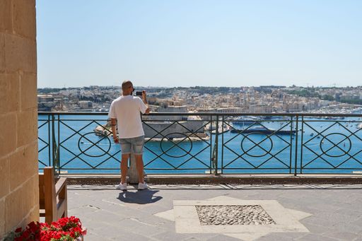 A male taking a picture of a beautiful view of Malta from a balcony