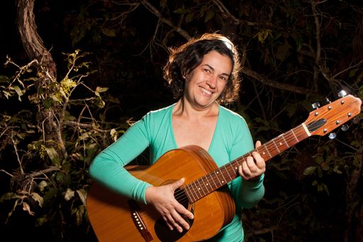 Happy Mature woman playing and singing with her acoustic guitar in the park