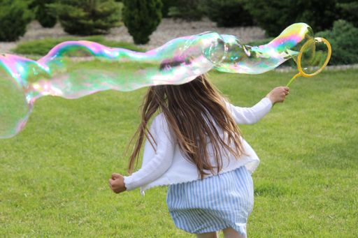 A closeup of a female child playing with giant bubbles in a park
