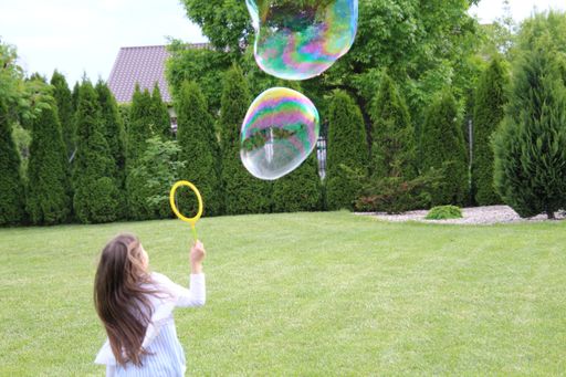 A closeup of a female child playing with giant bubbles in a park