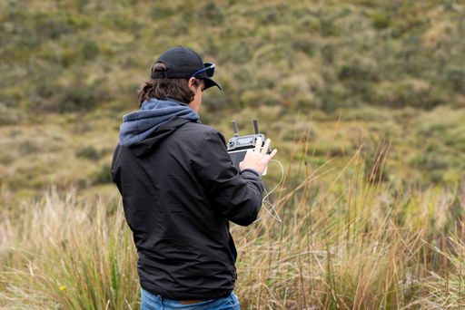 A young Hispanic man in a cap flying and operating a drone in a field during the daytime