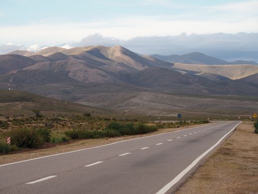 An empty road surrounded by dry fields and hills during daylight