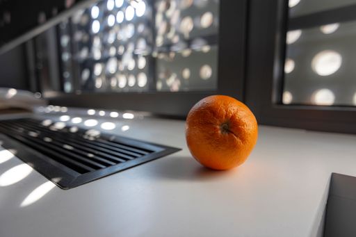 A closeup shot of an orange on the table, near the window, with bokeh sunlight in the background