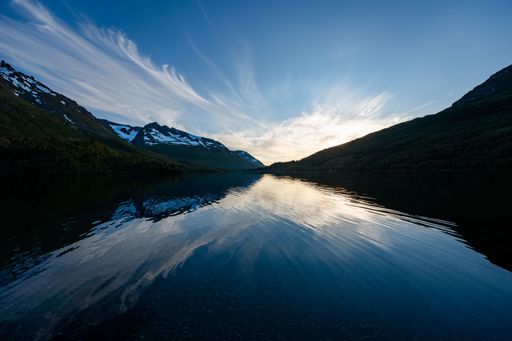 A Landscape of mountain range with snowy peaks reflecting on a lake against sunset sky