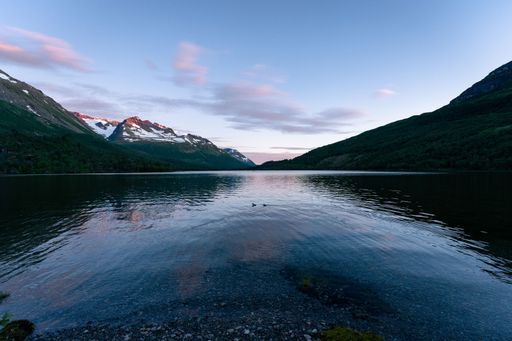 A landscape of mountain range with snowy peaks and green valleys reflecting on a lake