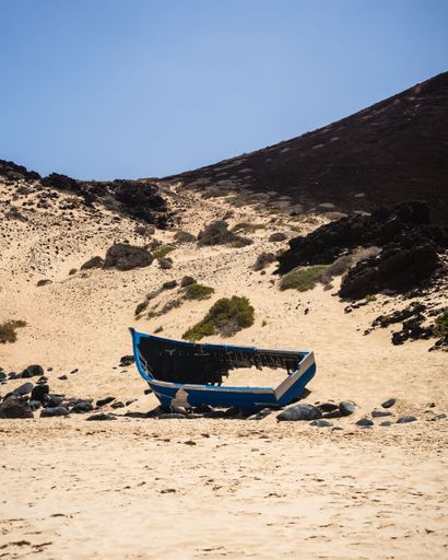 A vertical shot of a broken boat on the sandy hillside. Playa de las Conchas, Spain.