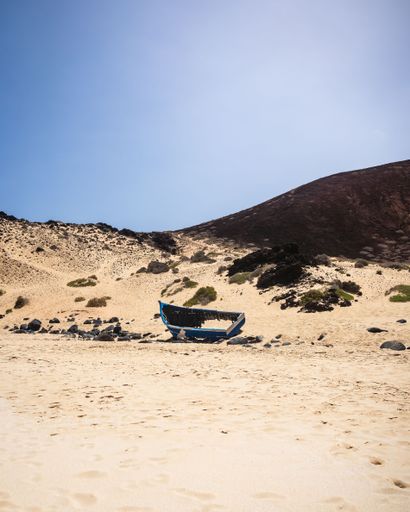 A vertical shot of a broken boat on the sandy hillside. Playa de las Conchas, Spain.