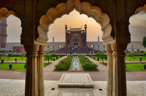 A view of Badshahi Mosque behind arch surrounded by growing palms during sunset