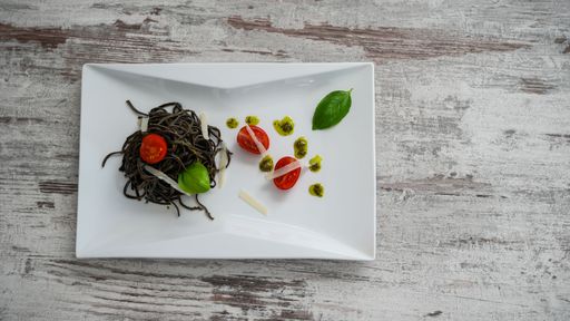 A top view of the black pasta with tomatoes in a white plate on a wooden surface