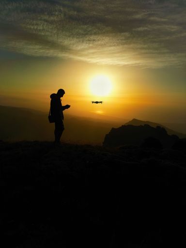 A vertical shot of a person's silhouette and a flying drone during sunset