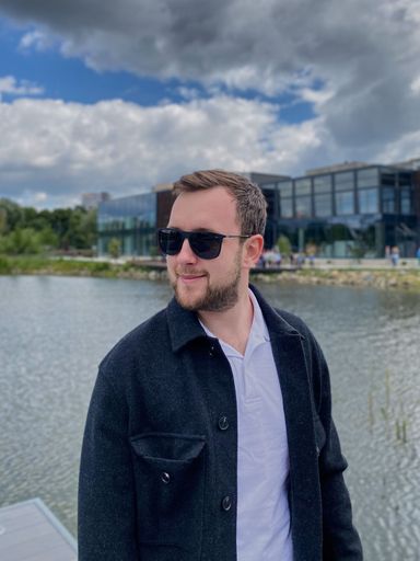 A vertical shot of a stylish Caucasian man posing near a river under a cloudy sky