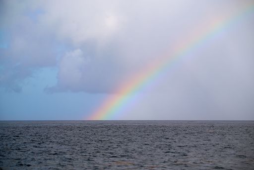A rainbow in front of the sea with a blue cloudy sky in the background, perfect for wallpapers