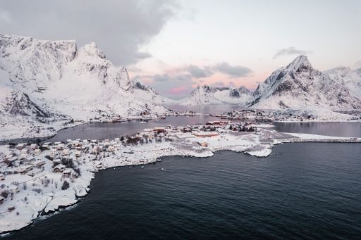 Aerial drone shot of the beautiful fishing village of Reine in the Lofoten islands during winter at sunset surrounded by snow covered mountains.