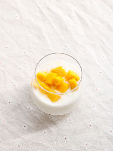A vertical closeup shot of delicious slices of mango with a milkshake in a glass on a white background