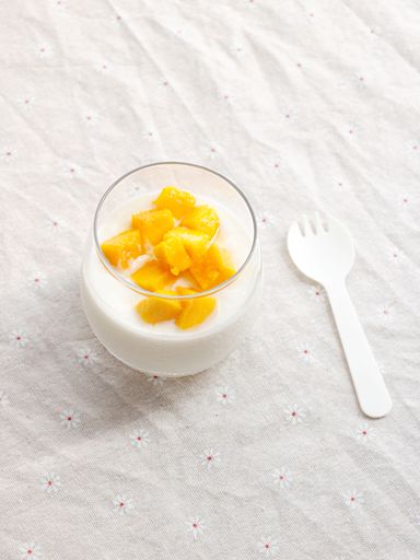 A vertical closeup shot of delicious slices of mango with a milkshake in a glass on a white background