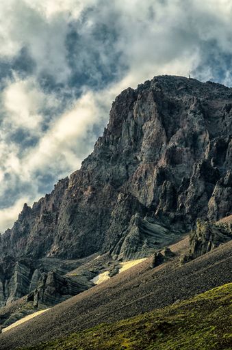 A vertical shot of rocky mountains in the wilderness under a cloudy sky on a sunny day