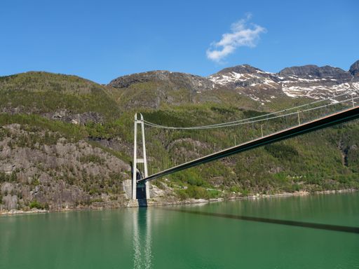 A bridge over lake surrounded by mountains and dense trees