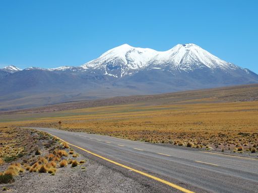 A beautiful shot of an empty road surrounded by fields and mountains covered in snow during daylight