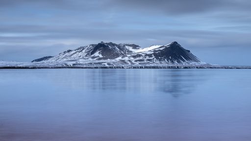 A beautiful shot of a snowy hill with a lake in the foreground