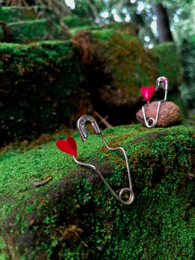 A vertical closeup shot of two pins with red hearts on the mossy rock