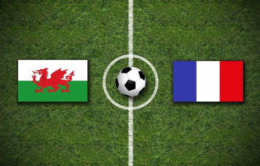 A high angle shot of the flags of France and Wales with a soccer ball in the center on a soccer field