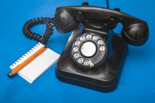 A black old phone with a notebook and a pen on blue background
