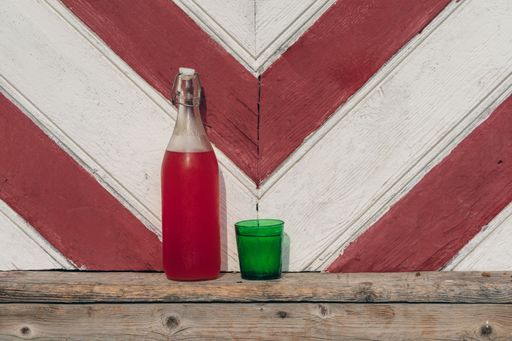 A bottle of fresh homemade rhubarb juice and glass against a wooden wall