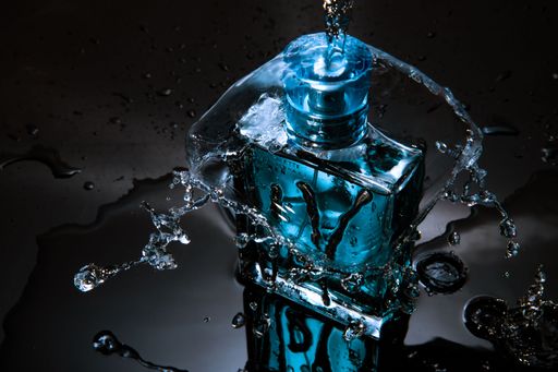 A beautiful shot of a Ulric De Varens Blue Eau De Toilette Perfume with water splashing over it on a dark background