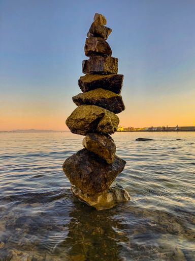 A vertical shot of a tower of stones at the shore at soft sunset