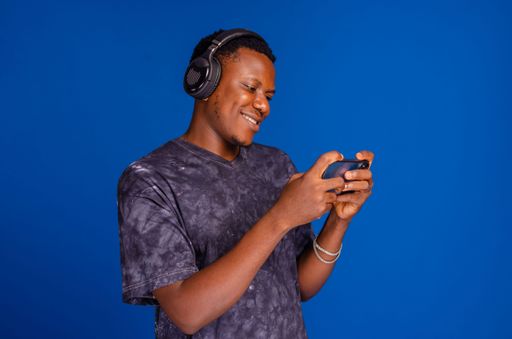 A happy Nigerian man listening to music on his headphone isolated on a blue background