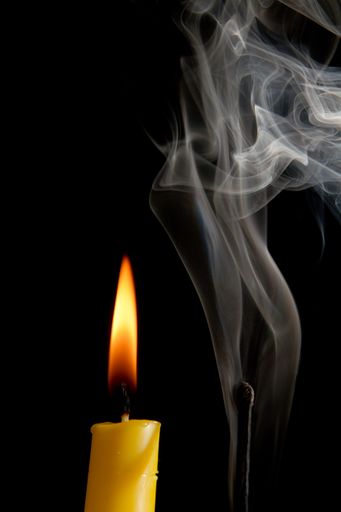 A vertical shot of a burnt out match with smoke and a lit candle isolated on a black background