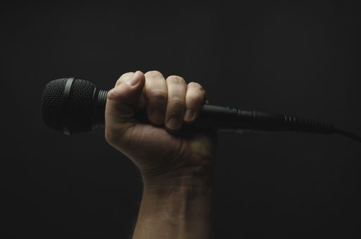 A person holding a black microphone on a black background