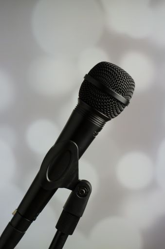 A vertical shot of a person holding a black microphone on a grey background with white bokeh lights