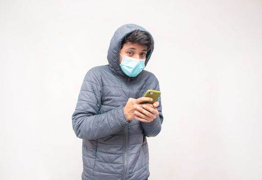 A portrait of young man holding his smartphone while having cold on a white background