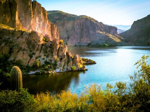 A gorgeous view of a serene pond in a sunny wilderness surrounded by rocky cliffs and cacti