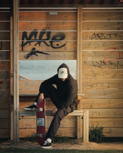 A skater sitting on a bench in front of the wooden wall in graffiti.