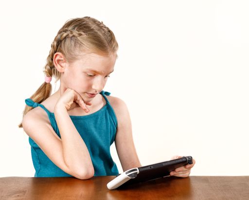 A young Caucasian girl watching at the tablet on a wooden table