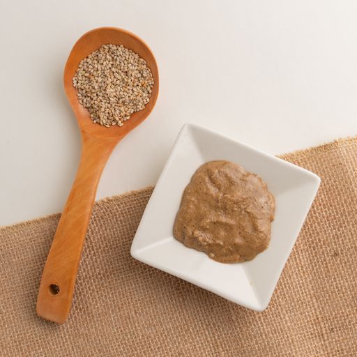 A top view shot of big wooden spoon with seeds and a small white plate with sauce