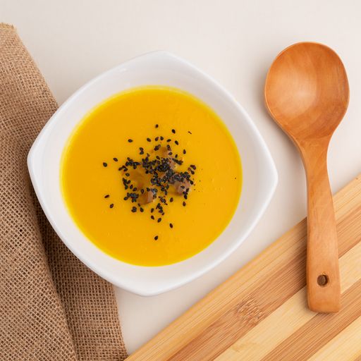 A high angle shot of pumpkin soup with sesame next to a big wooden spoon on a white table