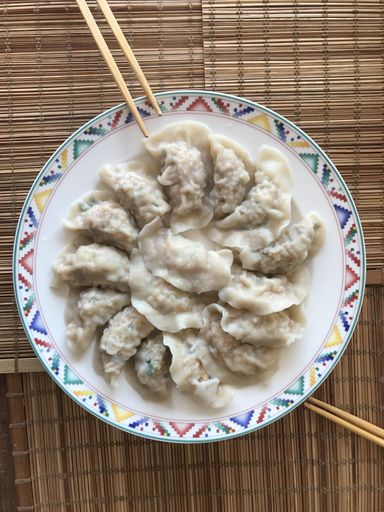 A high angle closeup shot of Chinese dumplings in a white plate with patterns next to chopsticks