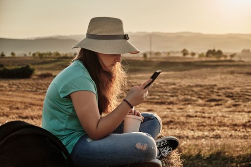 A selective focus shot of a young girl with round hat sitting and looking at the phone