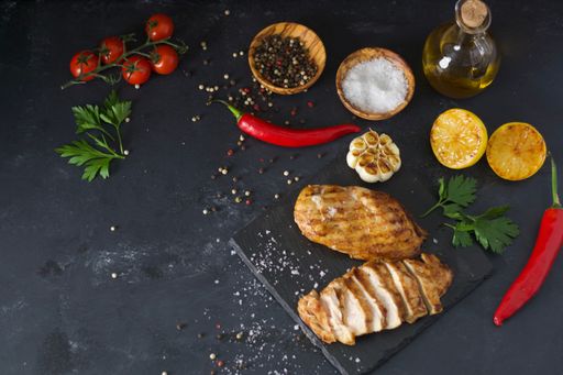A flat ray of cooked chicken fillet with colorful vegetables and seasonings on wooden surface