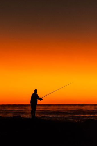 A silhouette of a fisherman with his fishing rod at sunrise on the beach