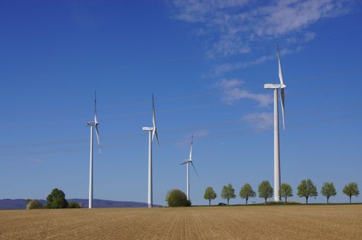 Wind turbines of Mainova in the north of Frankfurt in the agricultural landscape in front of a blue sky with high-voltage power lines.