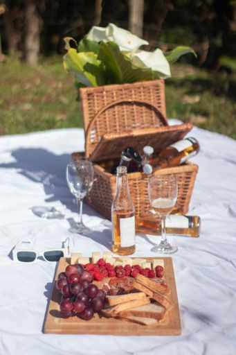 A vertical shot of a picnic basket, food board and wine outdoors on a white blanket