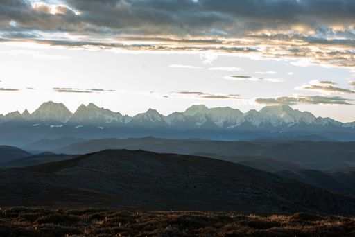 Sunlit clouds over a snow-covered mountain range surrounded by fields