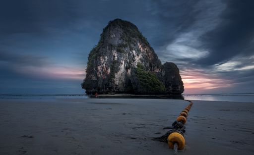A shot of a cliff on an ocean shore with a rope on the ground and the dark blue sky during the sunset in the background