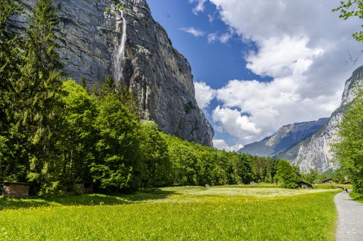 The image shows a valley with mountains rising on two sides and a waterfall on one side with a trail through the valley